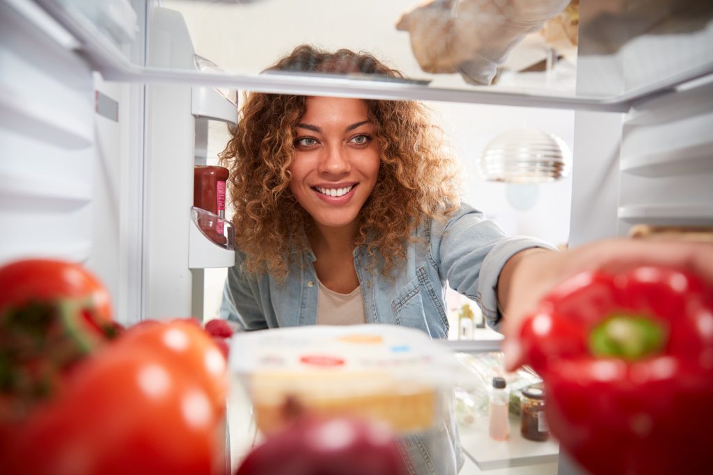 View Looking Out From Inside Of Refrigerator As Woman Opens Door And Unpacks Shopping Bag Of Food