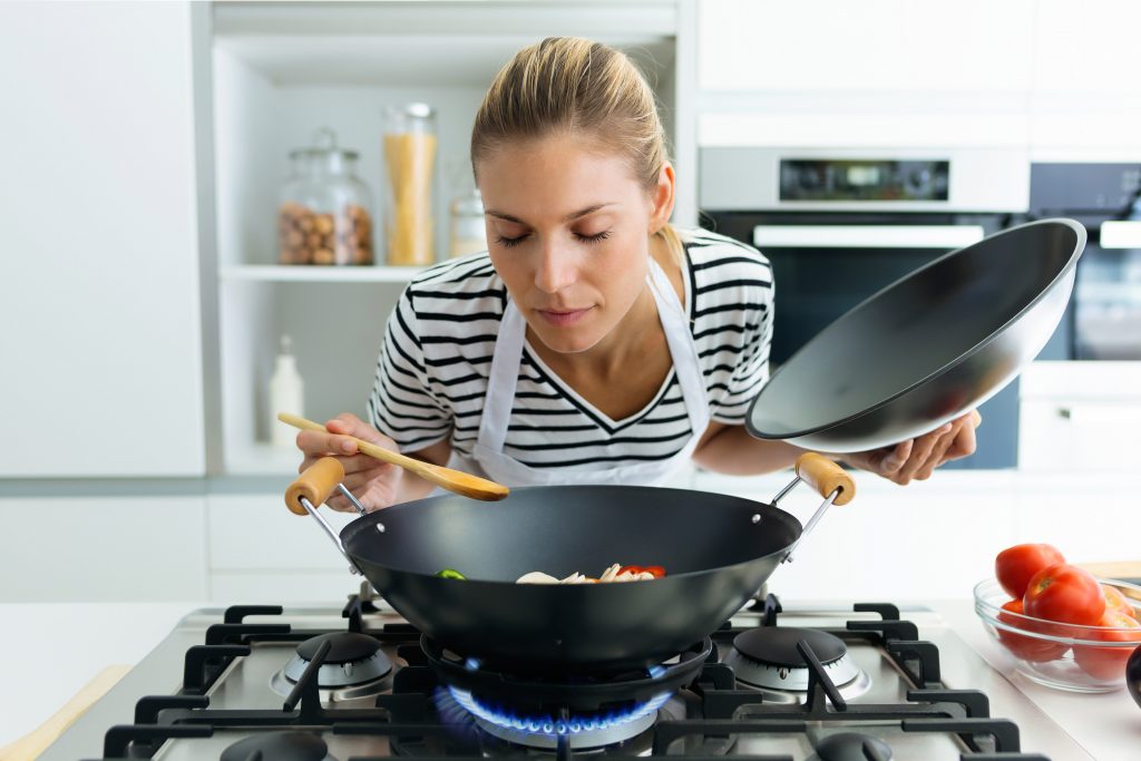 Shot of healthy young woman cooking and smelling food in frying pan in the kitchen at home.